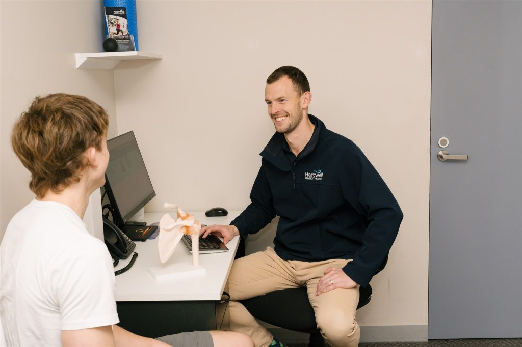 Physiotherapist showing a shoulder joint model to a patient while explaining shoulder dislocation, rehabilitation, and recovery.